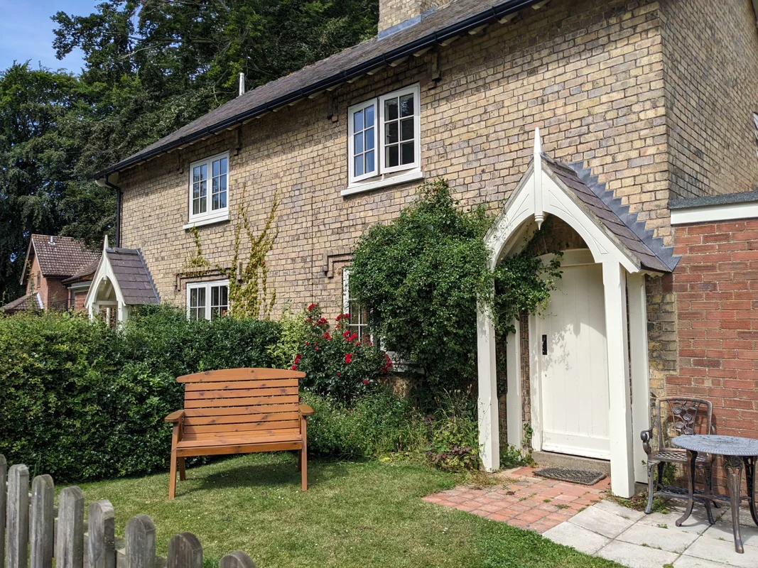 Stone cottage with garden bench, roses, and arched door. Sunny garden scene.