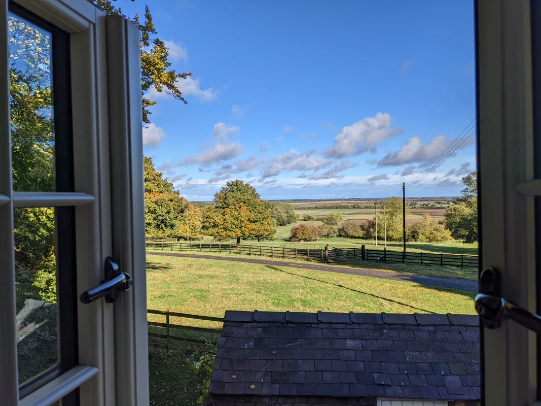 Open window framing lush green fields, trees, and blue sky with clouds