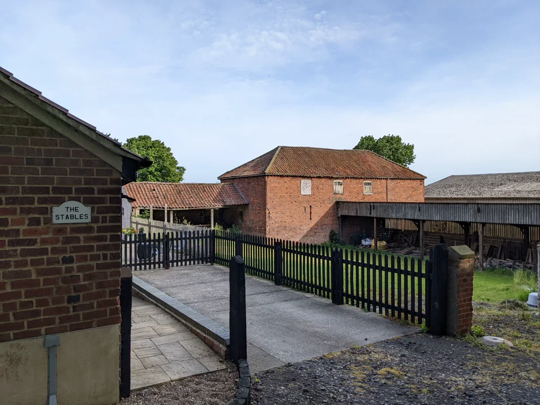 Brick stable building with 'The Stables' sign, fenced courtyard, garden, and cottage